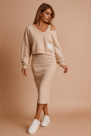 Gebreide two-piece set met V-hals trui en kokerrok in beige, met off-shoulder detail en casual sneakers.