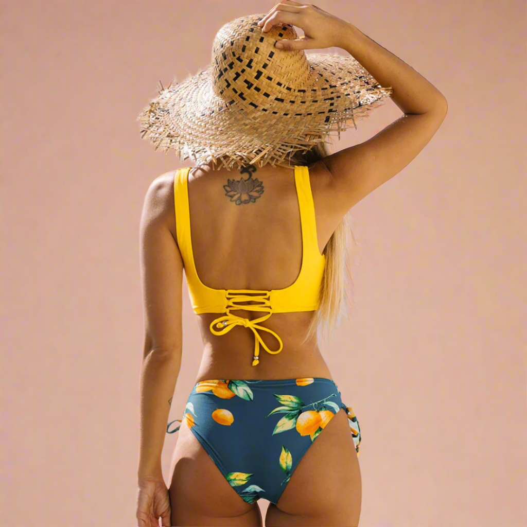Bikini met gele twist-top en donkerblauwe slip met vrolijke sinaasappelprint en vetersluiting op de rug.