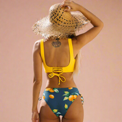 Bikini met gele twist-top en donkerblauwe slip met vrolijke sinaasappelprint en vetersluiting op de rug.