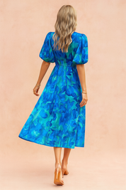 Blauwe midi-jurk met grote bloemprint, V-hals, pofmouwen en gesmokte taille.