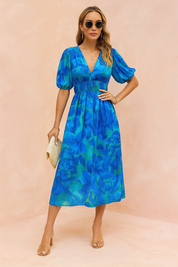 Blauwe midi-jurk met grote bloemprint, V-hals, pofmouwen en gesmokte taille.