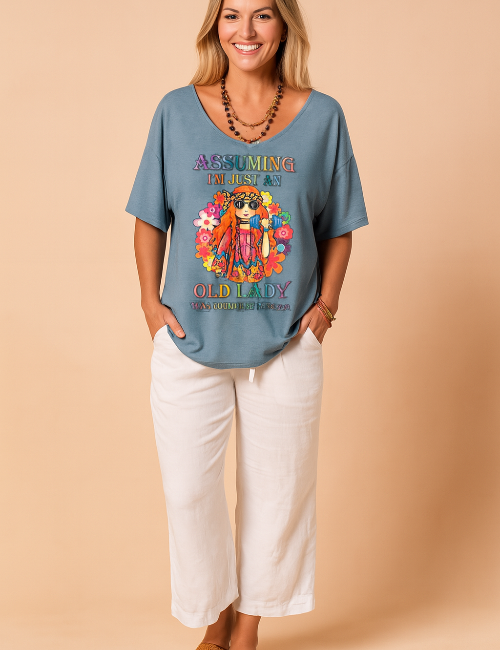 Blauwgrijs dames-T-shirt met diepe V-hals en kleurrijke hippieprint inclusief bloemen en tekst “Assuming I’m just an old lady”, gemaakt van luchtige, soepele stof voor een relaxte zomerse pasvorm.