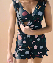 Zomer romper met wikkelmodel en bloemenprint op zwarte achtergrond, voorzien van speelse ruffle zomen.