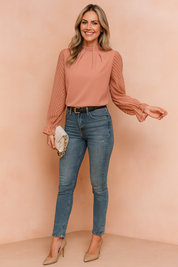 Blosroze blouse met geplooide hoge hals en zachte doorschijnende mouwen met visgraatmotief, afgewerkt met ruches voor een romantisch accent.