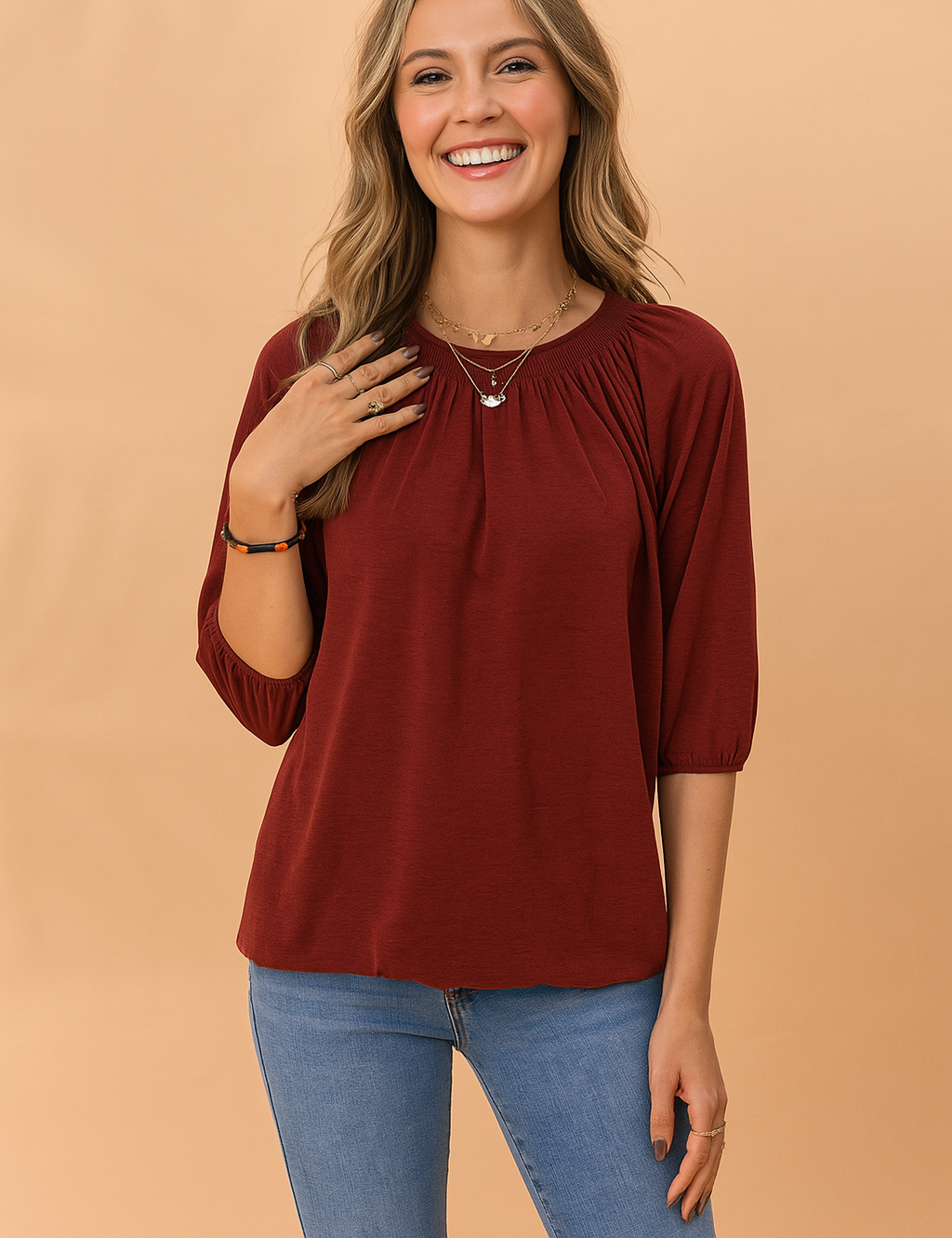 Bordeauxrode dames top met ronde halslijn en driekwartmouwen, afgewerkt met subtiele plooien bij de hals voor een flatterende en elegante uitstraling. Gemaakt van een zachte jersey stof met een losse, comfortabele pasvorm en elastische mouwboorden.