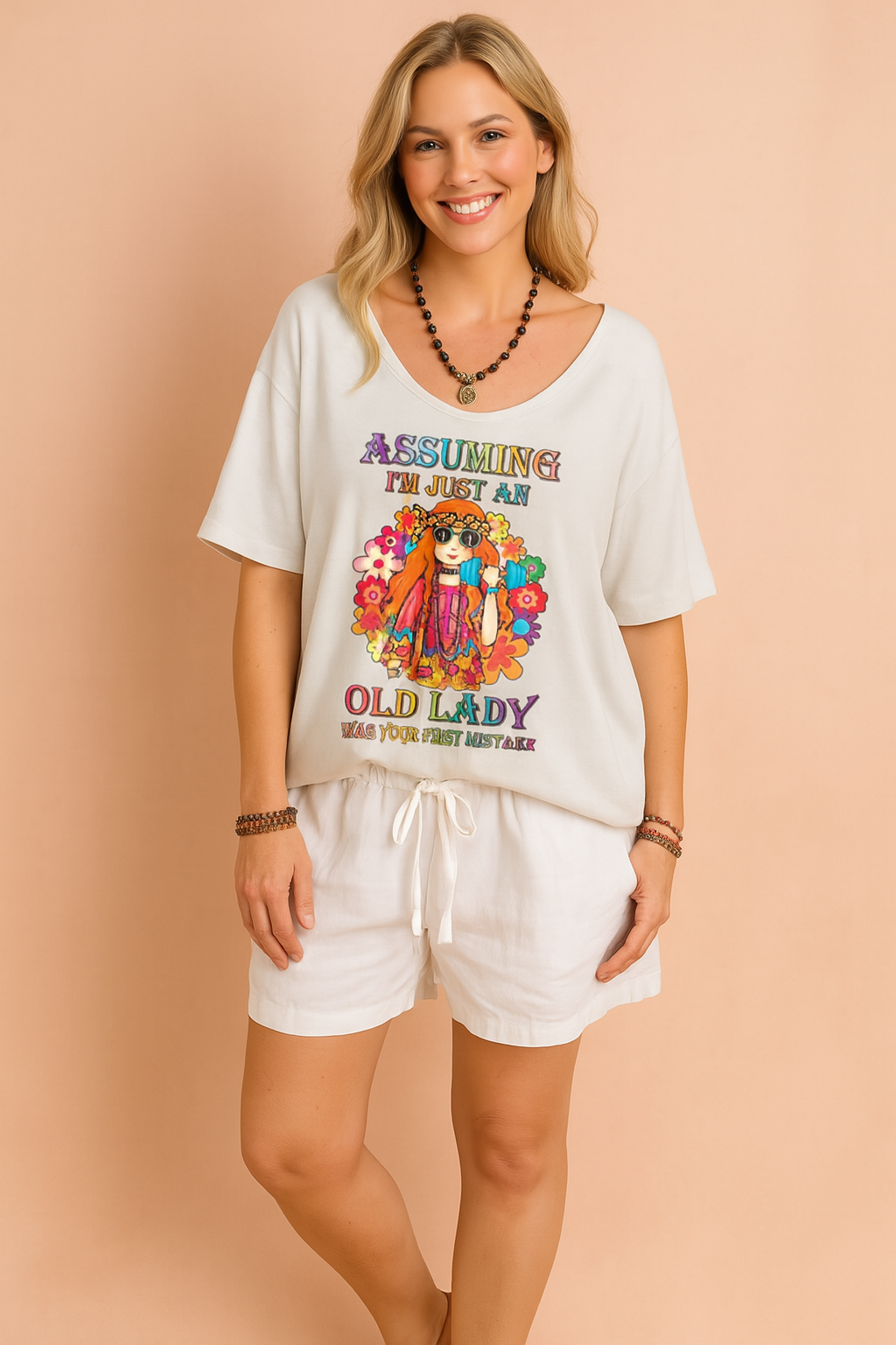 Crèmekleurig dames-T-shirt met diepe V-hals en opvallende kleurrijke hippieprint en tekst “Assuming I’m just an old lady”, vervaardigd van een luchtige stof en casual fit voor een relaxte zomerse look.
