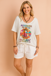 Crèmekleurig dames-T-shirt met diepe V-hals en opvallende kleurrijke hippieprint en tekst “Assuming I’m just an old lady”, vervaardigd van een luchtige stof en casual fit voor een relaxte zomerse look.