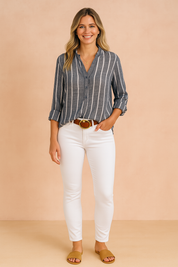 Gestreepte donkerblauwe linnen blouse met witte verticale strepen, lange mouwen en knoopsluiting, gestyled met een witte broek.