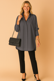 Diepgrijze lange blouse in los model met klassieke kraag en subtiele knoopsluiting. Elegant te combineren voor zakelijke en alledaagse outfits.