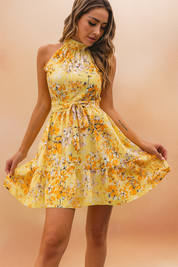 Vrouw draagt gele bloemen halternek mouwloze mini jurk met taille strik