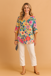 Vrouwelijke blouse met levendige bloemenprint in roze, oranje en blauw op een zonnige gele achtergrond. Losvallend silhouet met V-hals en splitdetail.