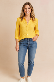 Mosterdgele linnen blouse met knopen en lange mouwen, gecombineerd met een middelblauwe high-waist jeans. De blouse heeft een casual pasvorm en luchtige stof.