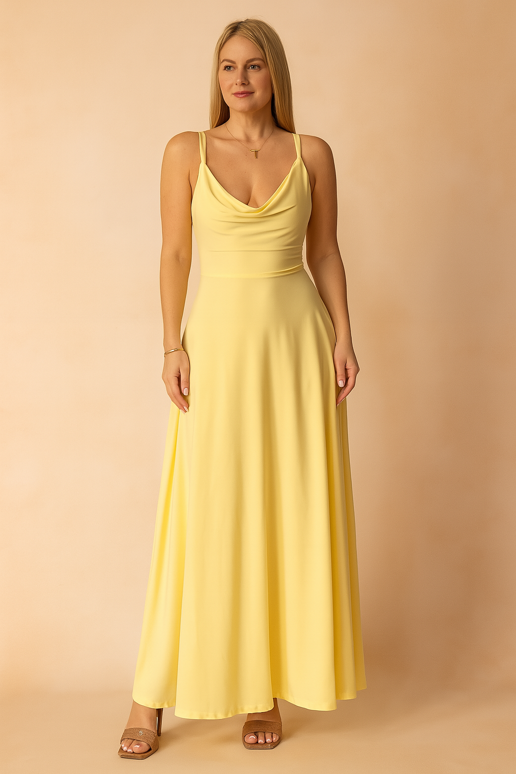 Gele maxi-jurk van gladde satijnachtige stof met watervalhals en smalle spaghettibandjes, geschikt voor zomer of strand.