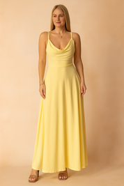 Gele maxi-jurk van gladde satijnachtige stof met watervalhals en smalle spaghettibandjes, geschikt voor zomer of strand.