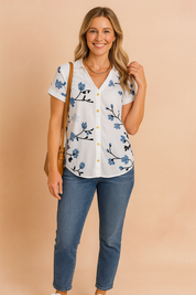 Witte blouse met korte mouwen, blauwe bloemenprint en gele knoopdetails – perfect voor alledaagse casual outfits.