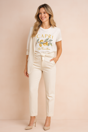 Wit T-shirt met citroenprint en “Capri”-opdruk in handgeschreven stijl, gecombineerd met een elegante crème outfit – frisse en verfijnde casual look.