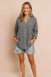Zachtgrijze linnen blouse met een los silhouet, diepe V-hals en drie witte knopen aan de voorkant. Gemaakt van luchtige linnenstof met een casual uitstraling en opgerolde mouwen.