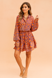 Korte jurk met oranje en paarse ikatprint, lange ballonmouwen, knoopsluiting en elastische taille, afgewerkt met een volantrok.