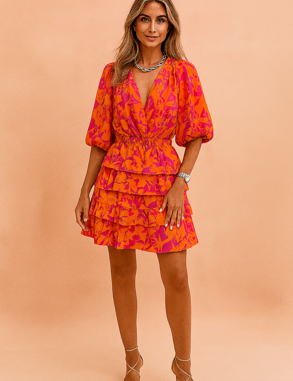 Korte zomerjurk met tropische bloemenprint in oranje en fuchsia, diepe V-hals, ballonmouwen en gelaagde rucherok voor een opvallende feestelijke look.