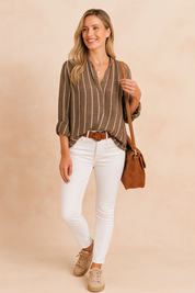Lichtbruine linnen blouse met beige verticale strepen, knoopsluiting en lange mouwen, gecombineerd met een witte skinny jeans en schoudertas.