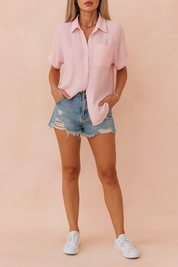 Lichtroze damesblouse met korte mouwen, gemaakt van een zachte geplisseerde stof met verticale ribbeltextuur. Uitgerust met een klassieke overhemdkraag, knoopsluiting aan de voorkant en een opgestikte borstzak links. De losvallende pasvorm zorgt voor een luchtige, casual stijl.
