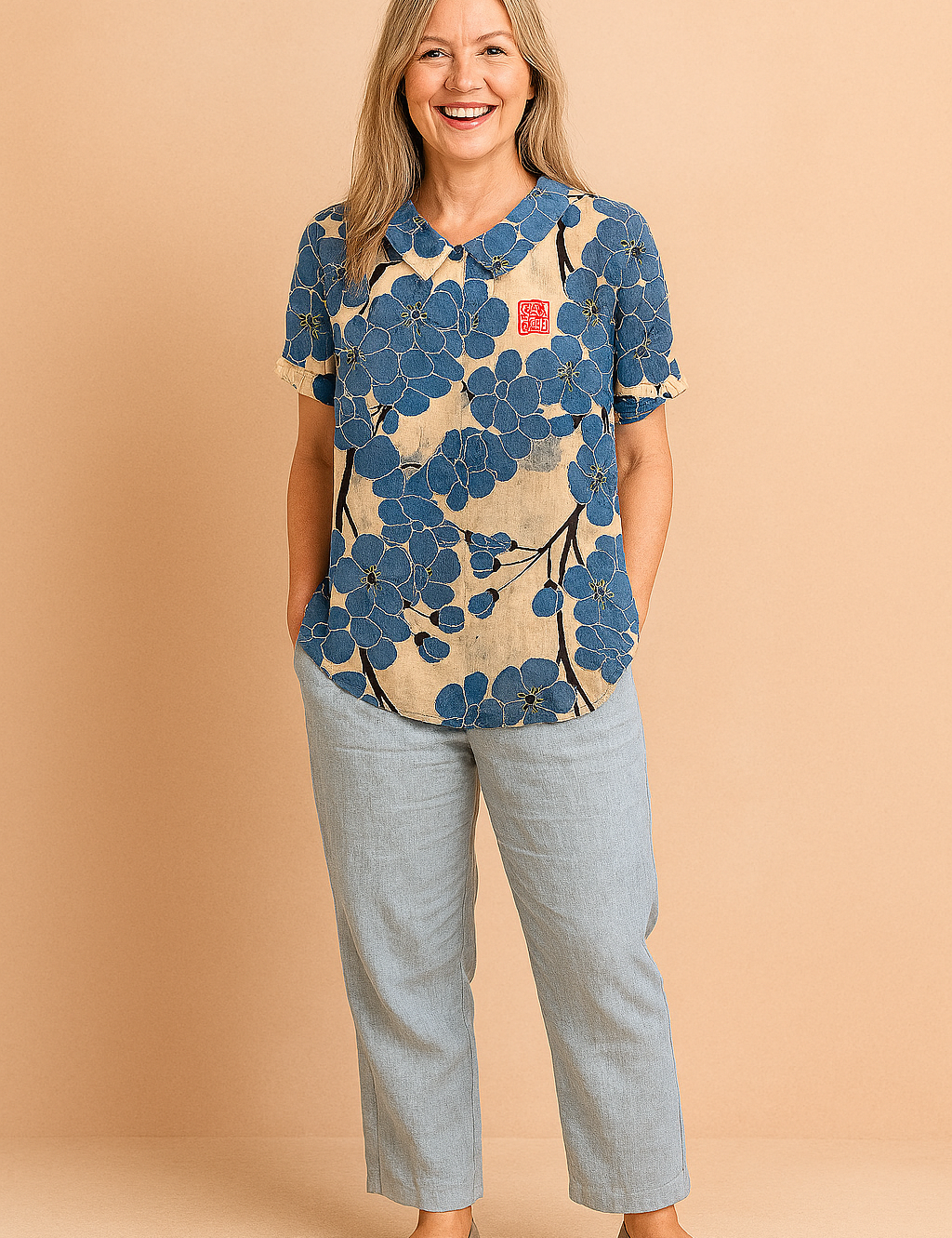 Beige linnen blouse met korte mouwen, opvallend grote blauwe bloemen en zwarte takken in een artistieke all-over print, voorzien van rood vierkant detail op de borst.