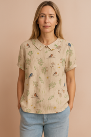 Beige linnen blouse met korte mouwen, Peter Pan-kraag en all-over vogelprint met botanische elementen.