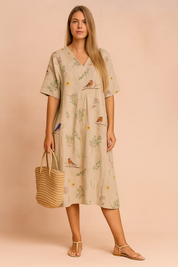 Beige midi-jurk van linnen met korte mouwen, V-hals en speelse vogelprint met groene bladeren en bloemen.