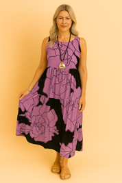 Mouwloze midi-jurk in paars met zwarte oversized bloemenprint, voorzien van speelse ruches en een luchtige pasvorm.