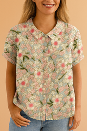 Korte mouwen blouse in zachte denimkleur met all-over print van roze en witte bloemen met groene bladeren, afgewerkt met een klassieke kraag.