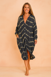 Oversized maxi jurk met tie-dye patroon in donkerblauw en beige, V-hals en knoopsluiting aan de voorkant.