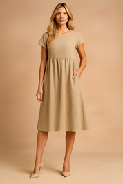 Beige midi zomerjurk met korte mouwen, hoge taille en steekzakken voor casual comfort.
