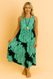 Mouwloze midi-jurk in aqua groen met zwarte oversized bloemenprint en gelaagde ruches voor een luchtige zomerse uitstraling.