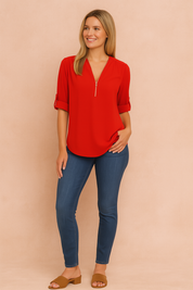 Blouse in helder rode kleur met gladde textuur, zilveren halve rits en V-halslijn. Mouwen zijn opgerold en vastgezet met knoopdetail.