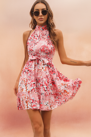 Vrouw draagt roze bloemen halternek mouwloze mini jurk met taille strik