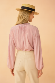 Roze damesblouse met subtiele verticale streepstructuur, gemaakt van een luchtige geweven stof. Voorzien van lange ballonmouwen met elastische manchetten, knoopsluiting aan de voorkant en een opstaand rufflekraagje met keyhole-detail. De losvallende pasvorm zorgt voor een vrouwelijke en stijlvolle uitstraling.