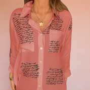 Roze blouse met zwarte handgeschreven tekstdetails en een losse pasvorm, voorzien van lange mouwen.