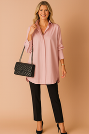 Lichtroze blouse in losvallend model met een klassieke kraag, lange mouwen en verborgen knopen. De soepele stof en lengte geven een verfijnde, vrouwelijke uitstraling.