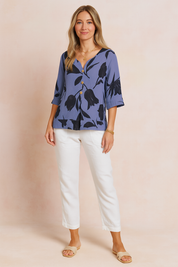 Blouse in stoffige blauwe tint met zwarte tulpenprint, korte zoom, driekwartmouwen en knoopsluiting aan de voorkant voor een moderne en luchtige uitstraling.