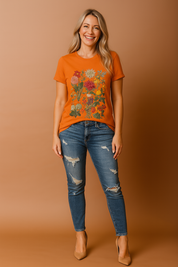 Oranje T-shirt met ronde hals en levendige bloemenprint in natuurlijke kleuren, waaronder rood, zalmroze, geel en groen, in een symmetrische opstelling op het midden van het shirt.