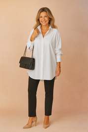 Tijdloze oversized blouse in helder wit met lange mouwen, klassieke kraag en verborgen knoopsluiting. Valt ruim over de heupen voor een elegante en veelzijdige pasvorm.