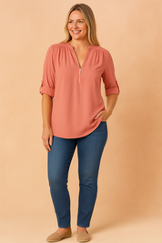 Vrouwelijke blouse in effen zalmroze tint, vervaardigd uit een lichtgewicht gladde stof. Met diepe V-hals en metalen rits, 3/4-mouwen met vaste omslag.