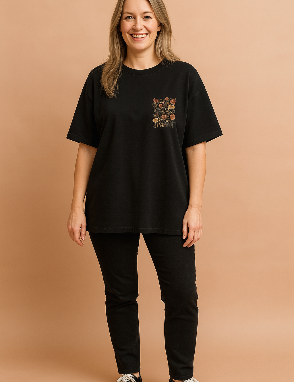 Zwart dames T-shirt met ronde hals en korte mouwen, uitgevoerd in een losse pasvorm. Op de linkerborst bevindt zich een decoratief bloemenmotief in geborduurde stijl, met warme herfsttinten die contrasteren tegen de effen achtergrond. Gemaakt van zachte katoenen jersey, perfect voor casual dagelijks gebruik.