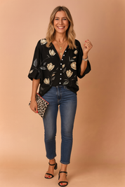 Elegante zwarte blouse met ivoorkleurige tulpenprint, diepe V-hals, pofmouwen en knoopsluiting aan de voorkant, gestyled voor een avondlook.
