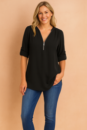 Effen zwarte damesblouse in soepele stof met V-hals en metalen halve rits aan de voorkant. De mouwen zijn nonchalant opgerold en vastgezet met een knoopsluiting.