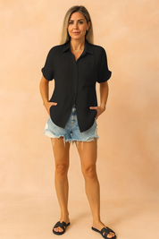Zwarte damesblouse met korte mouwen, gemaakt van een lichtgewicht geplisseerde stof met subtiele verticale ribbelstructuur. Voorzien van een klassieke overhemdkraag, knoopsluiting aan de voorkant en een borstzak links. Losvallend model, perfect voor een casual en luchtige zomerse outfit.
