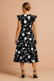 Zwarte midi-jurk met witte bloemenprint, V-hals, ruches aan de schouders en geplooide rok met ceintuur in de taille.