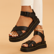 Zwarte platformsandalen met gekruiste bandjes, enkelondersteuning en gesp, voorzien van gele stiksels en grove zool.