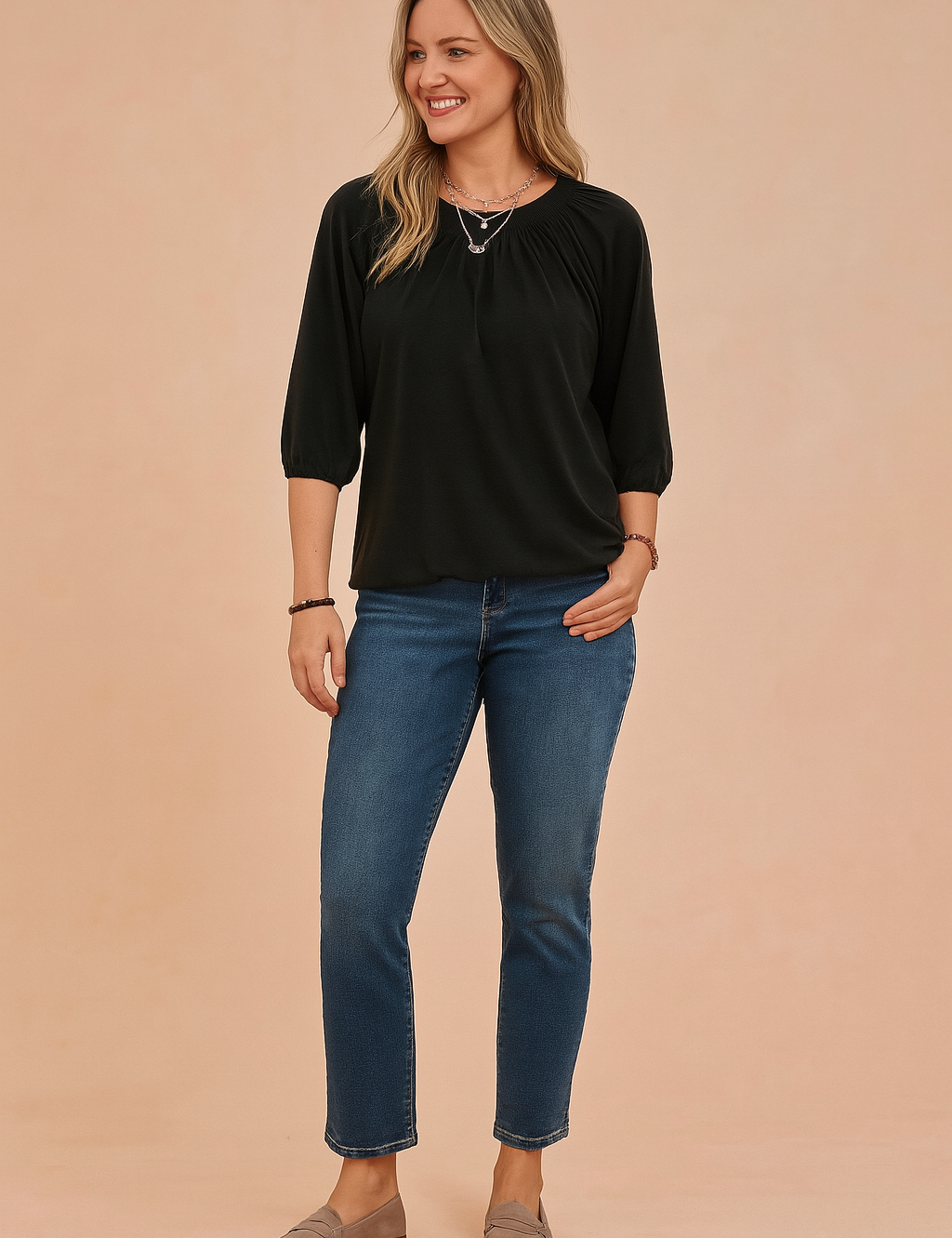 Zwarte dames top met ronde hals en driekwartmouwen, voorzien van elegante plooidetails rond de halslijn en licht gepofte mouwen met elastische boorden. Gemaakt van een soepele, effen jersey stof in een losvallende pasvorm die zowel comfort als een verfijnde uitstraling biedt.